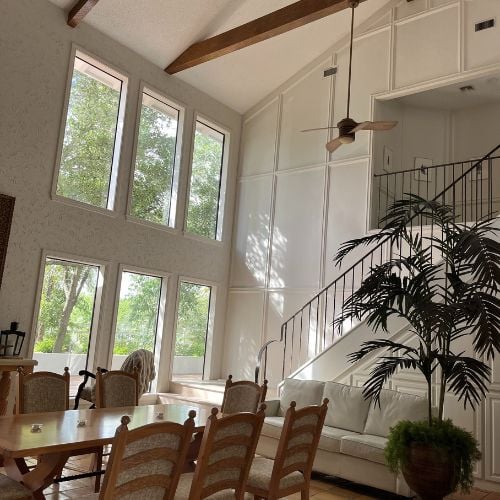 Bright interior with large windows, dining table, staircase, and houseplant