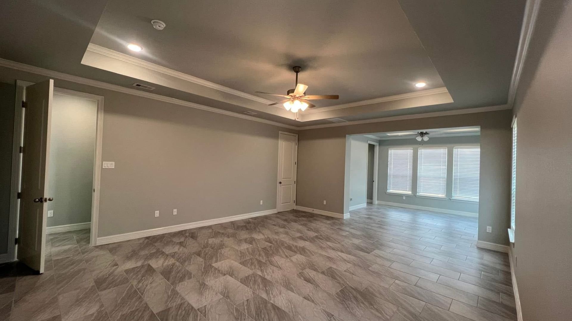 Empty room with tray ceiling, tile floor, and two ceiling fans
