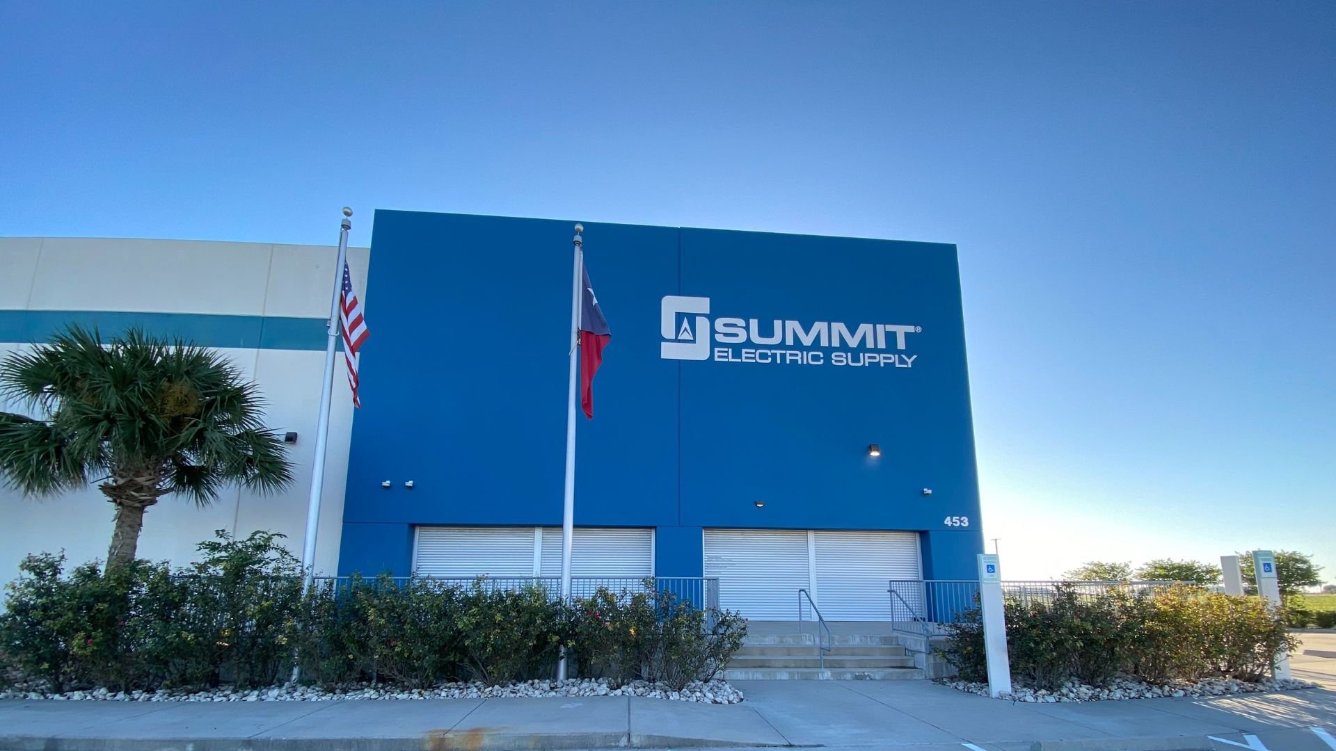 Summit Electric Supply building with US and Texas flags on blue exterior