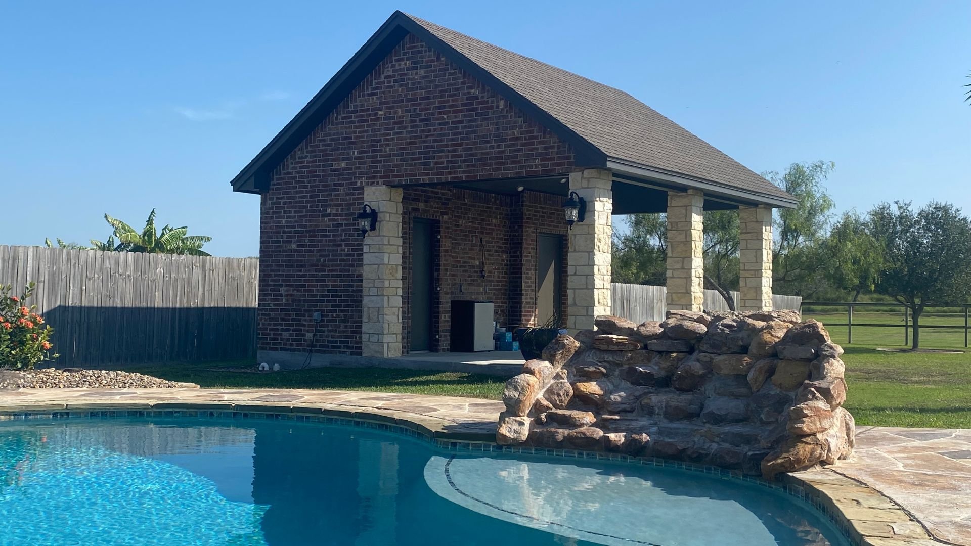 Brick pool house with stone columns next to blue swimming pool