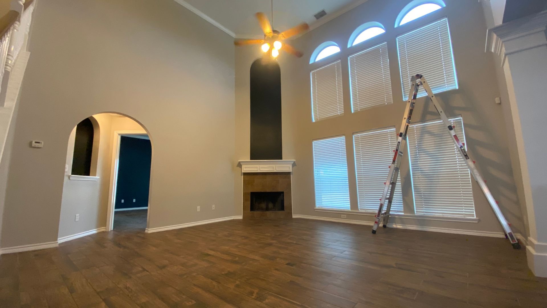 Empty room with hardwood floors, fireplace, arched doorway, and ladder