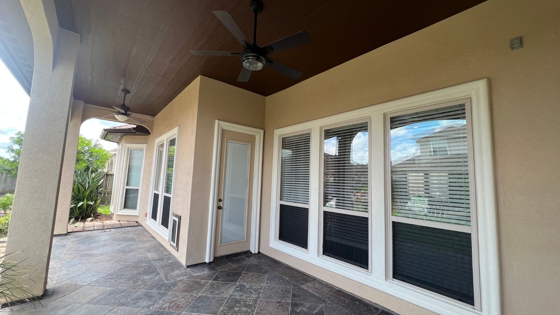 Covered patio with tiled floor, windows, door, and ceiling fan
