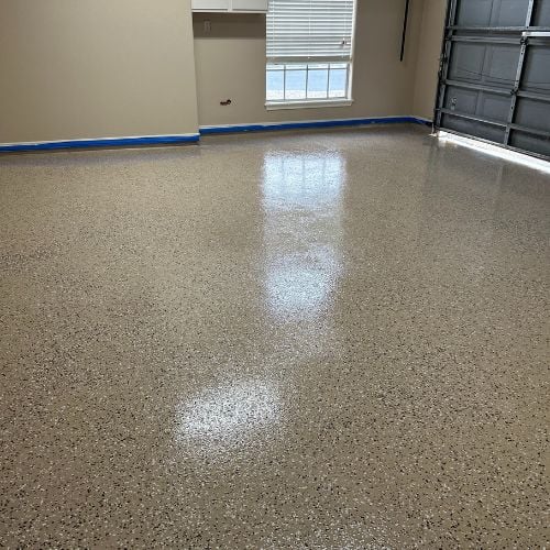 Newly installed epoxy garage floor with speckled finish and blue painter's tape