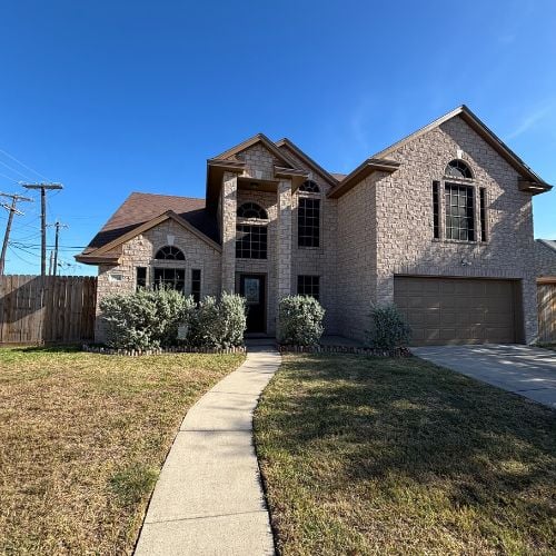 Stone two-story house with attached garage and concrete walkway